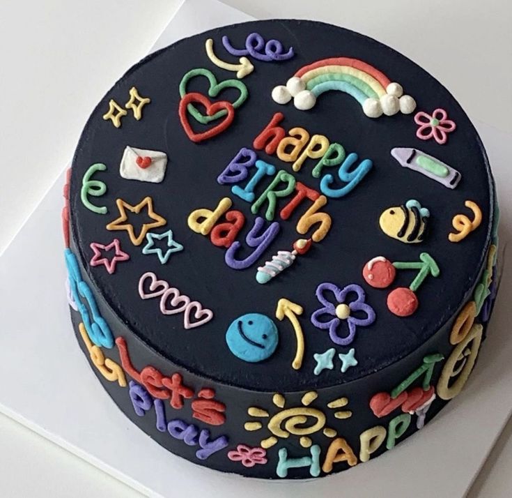 a birthday cake decorated with rainbows, stars, and other decorations on a white surface