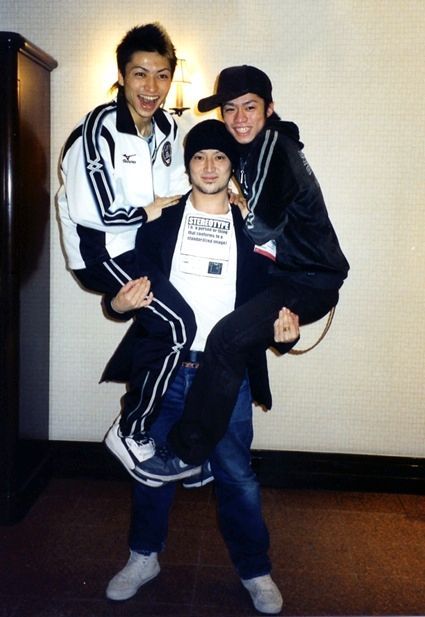 three young men posing for the camera in front of a wall