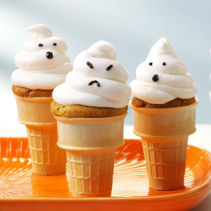 three cupcakes with white frosting and ghost faces on them sitting in cones