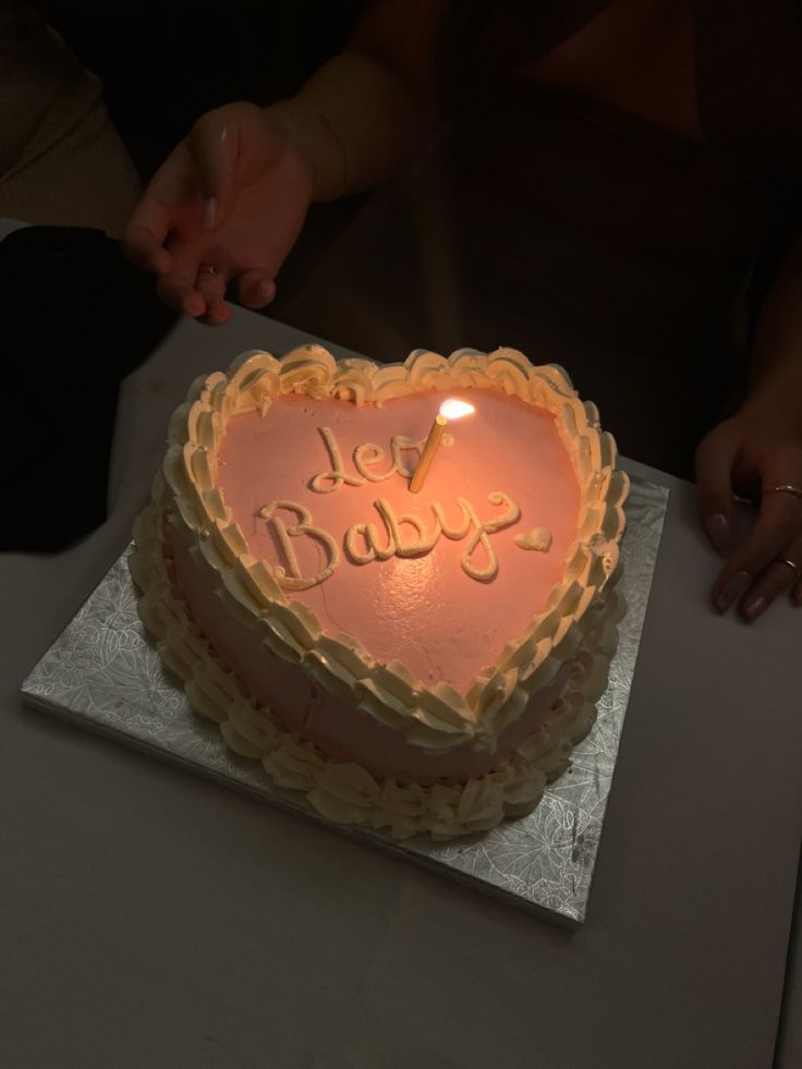 a heart shaped cake sitting on top of a table with someone holding a lit candle