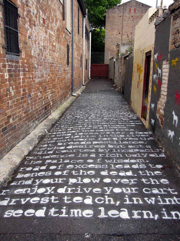 an alley way with graffiti written on the pavement and brick buildings in the background,