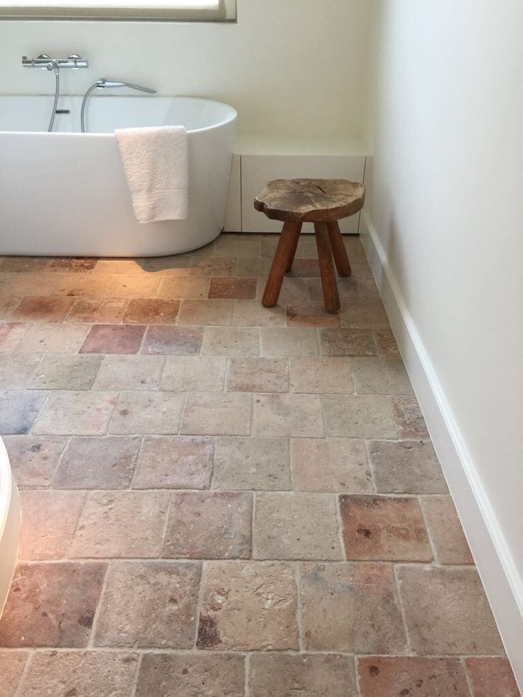 a white bath tub sitting under a window next to a wooden stool in a bathroom