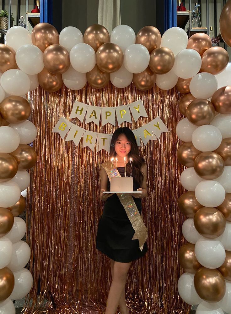 a woman standing in front of a birthday cake surrounded by balloons and streamers with the words happy birthday written on it