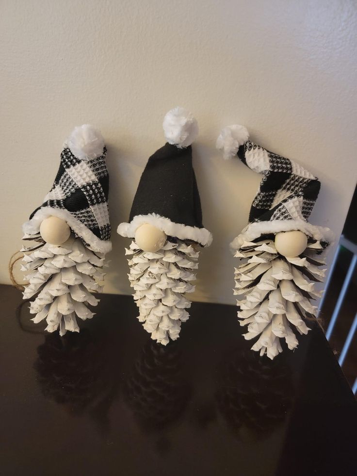 three pine cones with hats on them sitting on top of a black table in front of a white wall