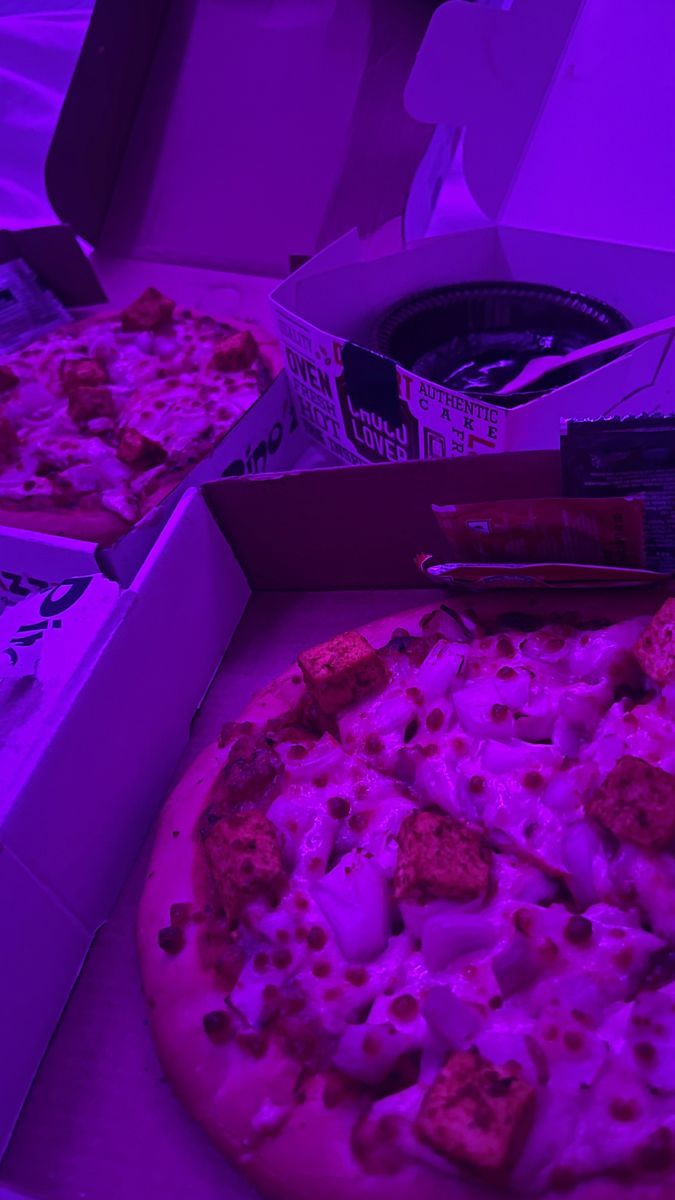 two pizzas are sitting in boxes on the table, one is purple and the other is red