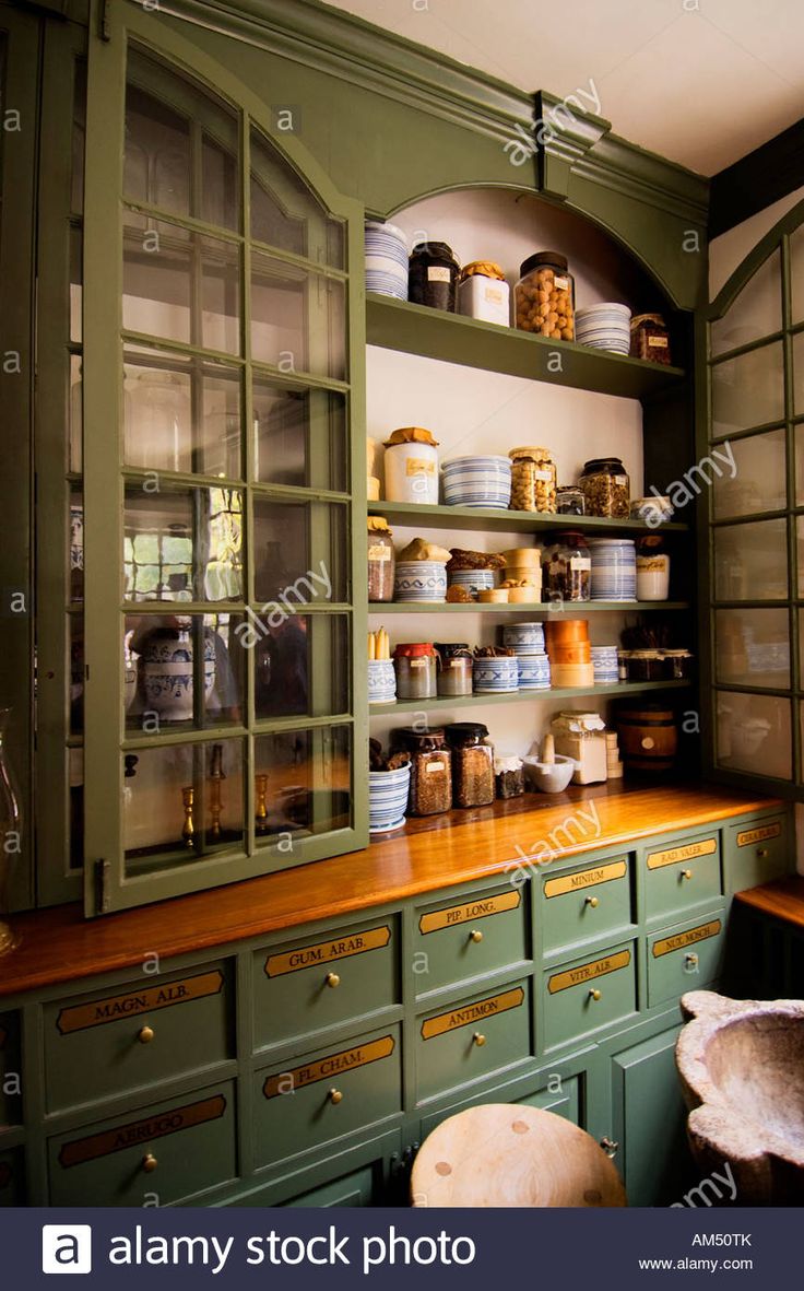 an old fashioned kitchen with green cabinets and wooden counter tops, filled with jars and pans