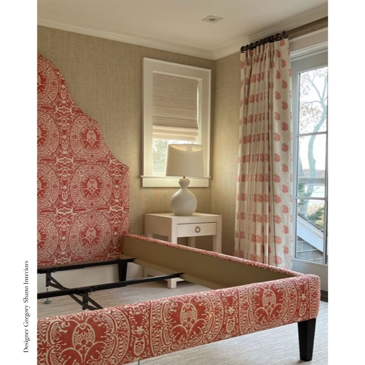 a bedroom with red and white bedding, window curtains, and an upholstered bench in front of a sliding glass door