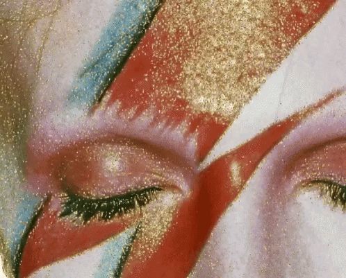 the eye of a woman with gold glitter on her face and eyelashes, as if it were painted to look like an abstract painting