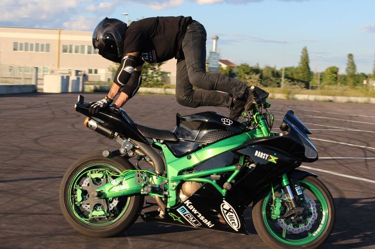 a man riding on the back of a green and black motorcycle in a parking lot