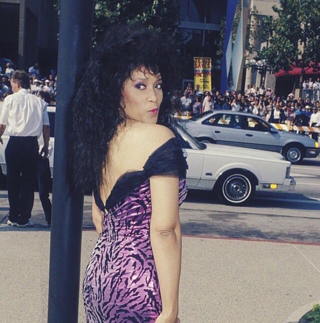 a woman standing next to a pole on the side of a road with people in the background