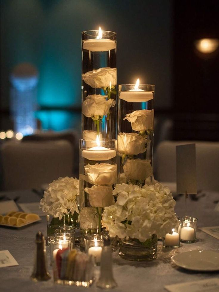 a tall vase filled with lots of white flowers and lit candles on top of a table