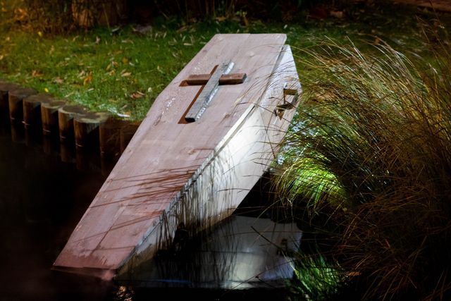 an old wooden boat with a cross on it is sitting in the water next to some grass