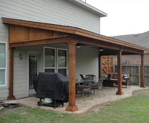 an outdoor covered patio with grill and table in the back yard next to a house