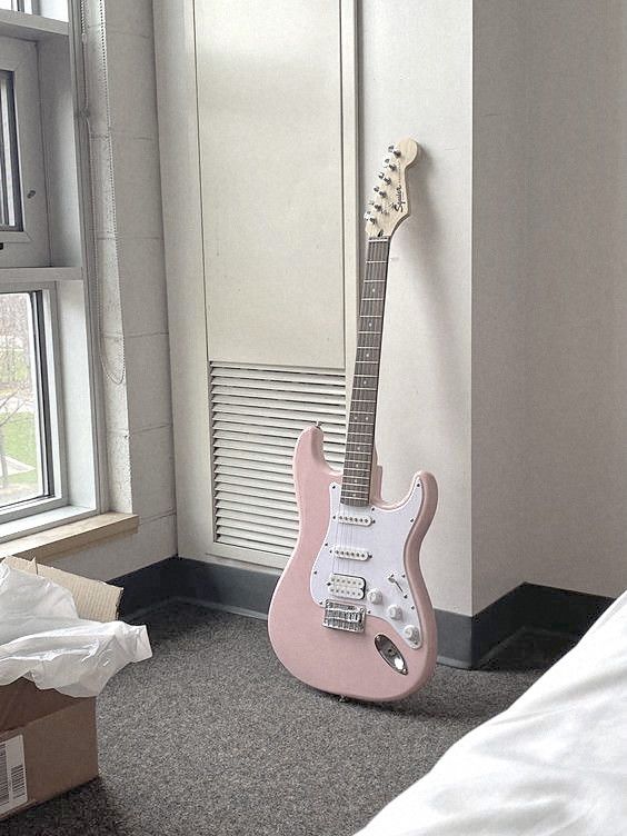 a pink guitar sitting on the floor next to a window