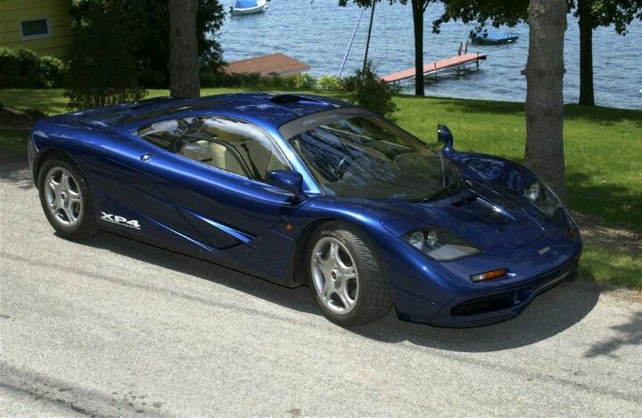 a blue sports car is parked on the side of the road near some trees and water