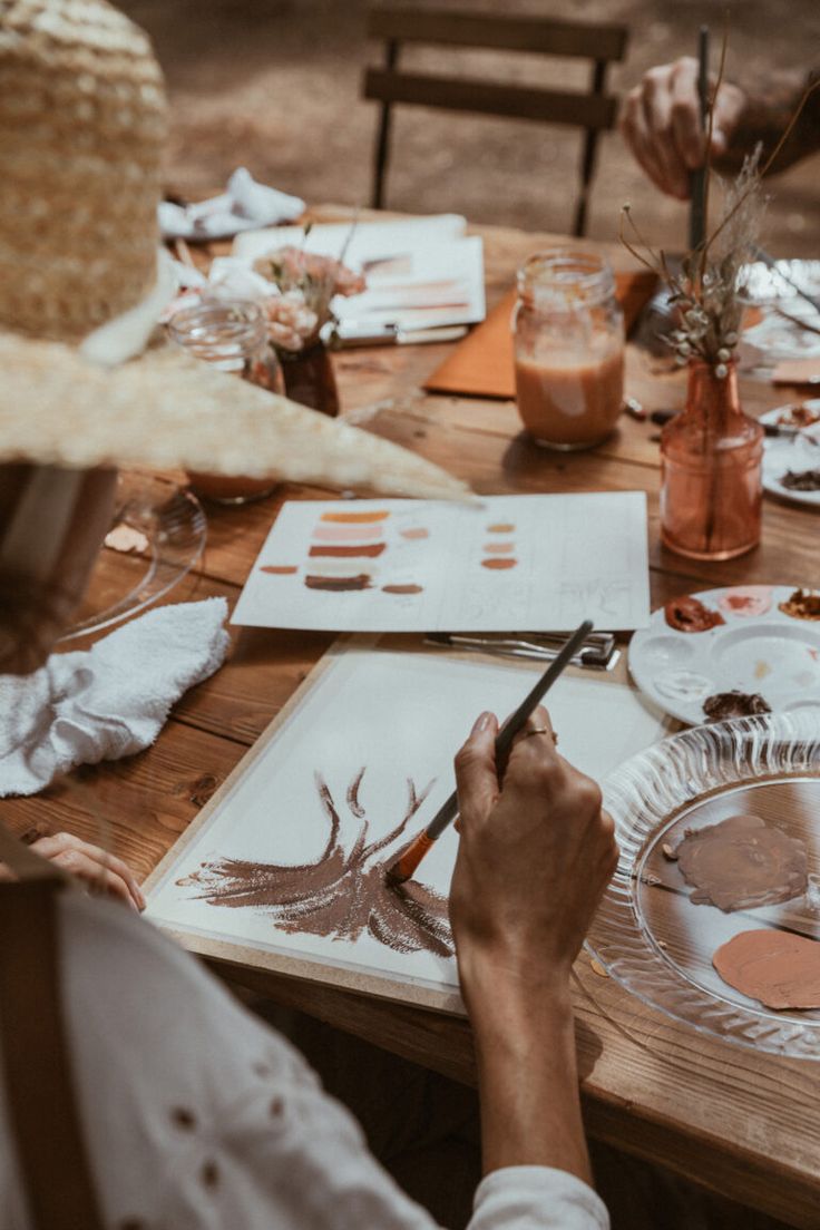 people sitting at a table with paper plates and paintbrushes in their hands as they draw designs