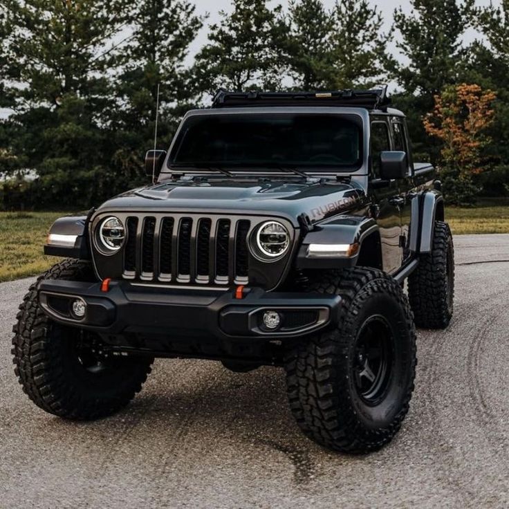 a black jeep parked on top of a parking lot next to some grass and trees