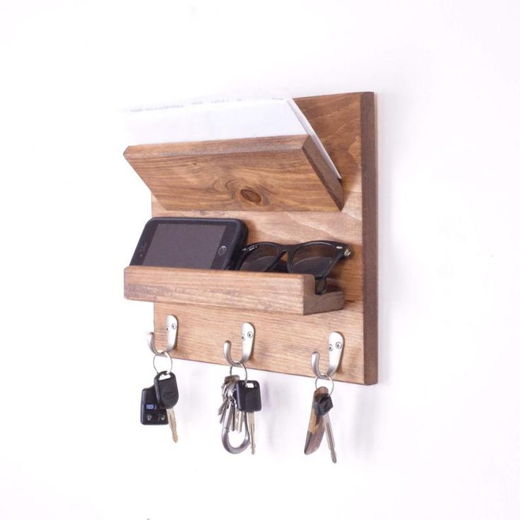 a wooden key holder with keys and cell phone on the hooks, attached to a wall