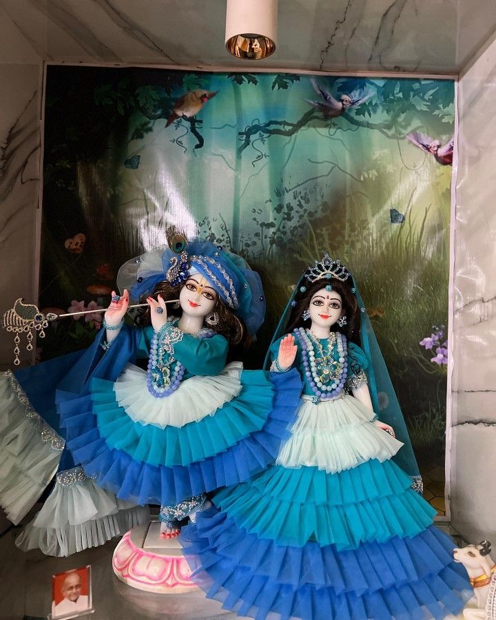 two dolls dressed in blue and white sitting on top of a table next to a wall