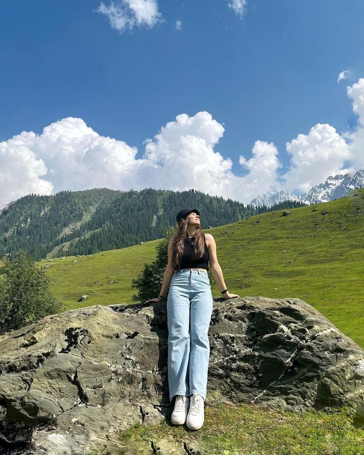 a woman standing on top of a large rock in the middle of a green field