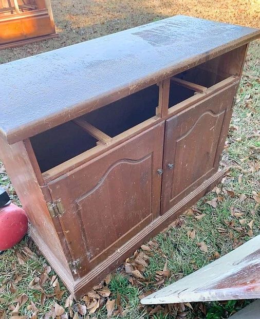 an old wooden cabinet sitting on top of grass next to a red fire hydrant