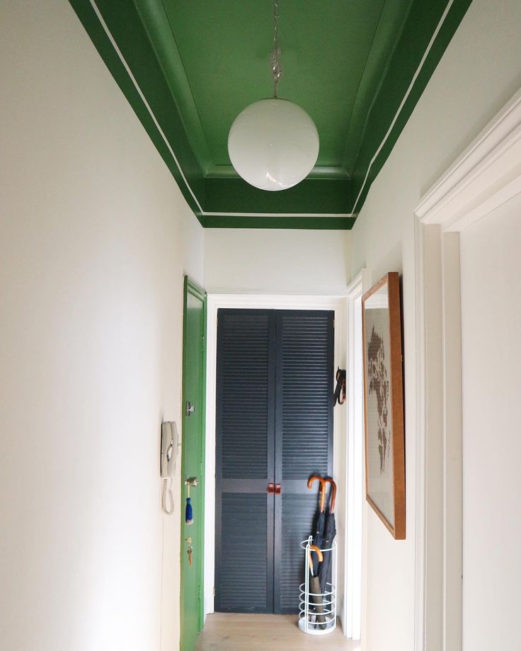 an empty hallway with green painted ceiling and white walls, two umbrellas hanging on the door