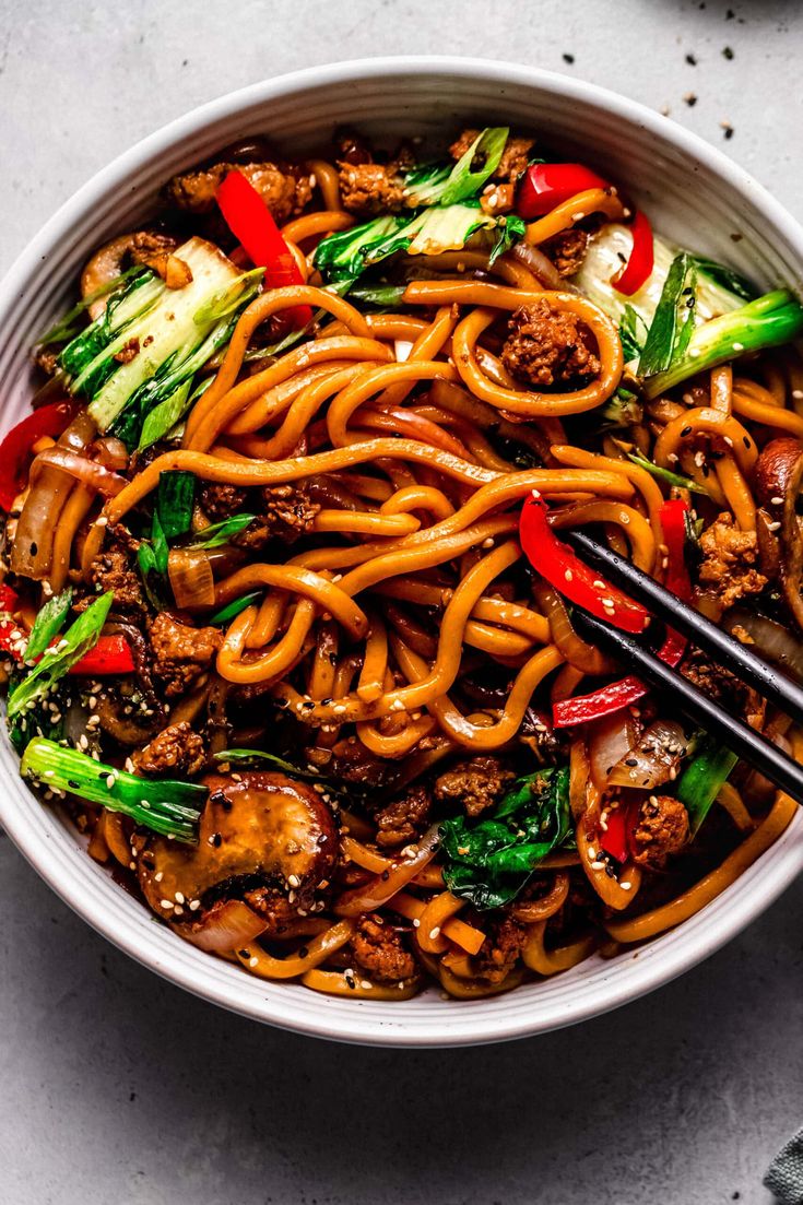 a bowl filled with stir fry noodles and vegetables on top of a table next to chopsticks