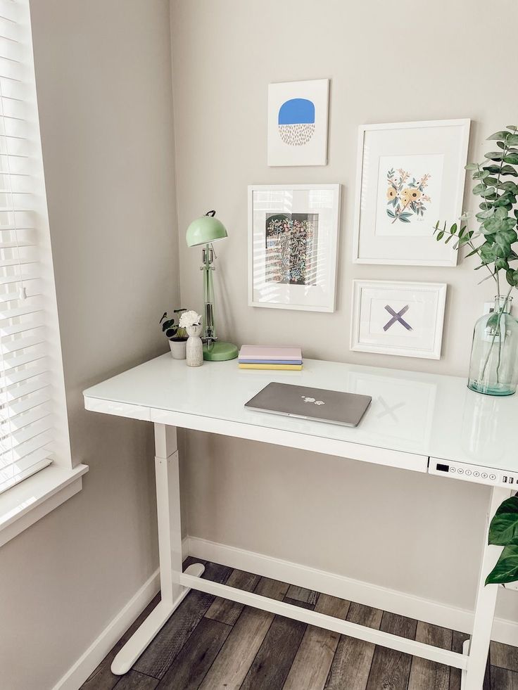 a white desk topped with a laptop computer next to a plant and pictures on the wall