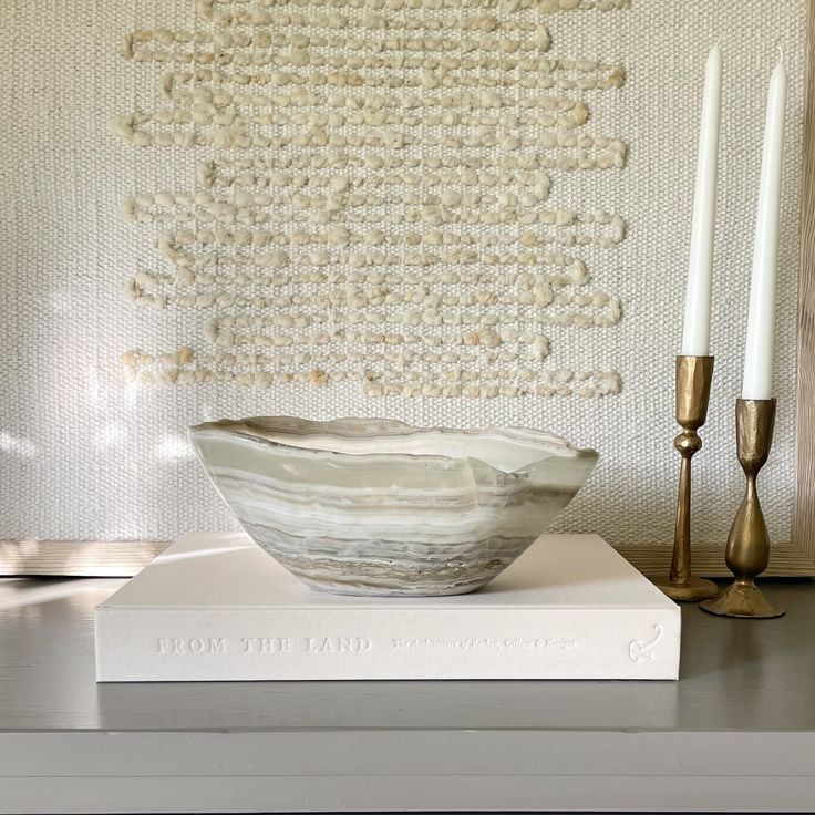 a white bowl sitting on top of a table next to two candles and a book