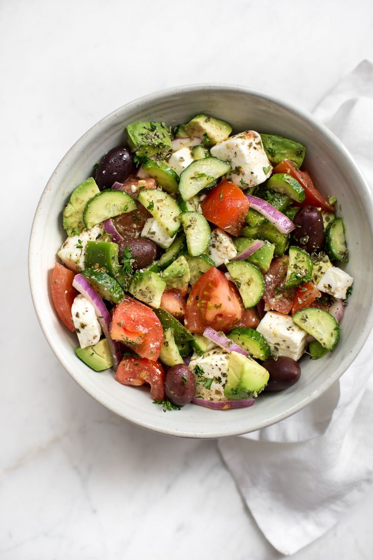 a white bowl filled with cucumber, tomato and feta cheese salad on top of a marble counter