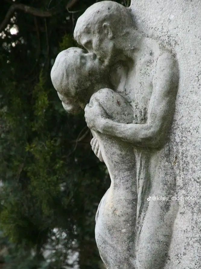 a stone statue holding a baby next to a tree