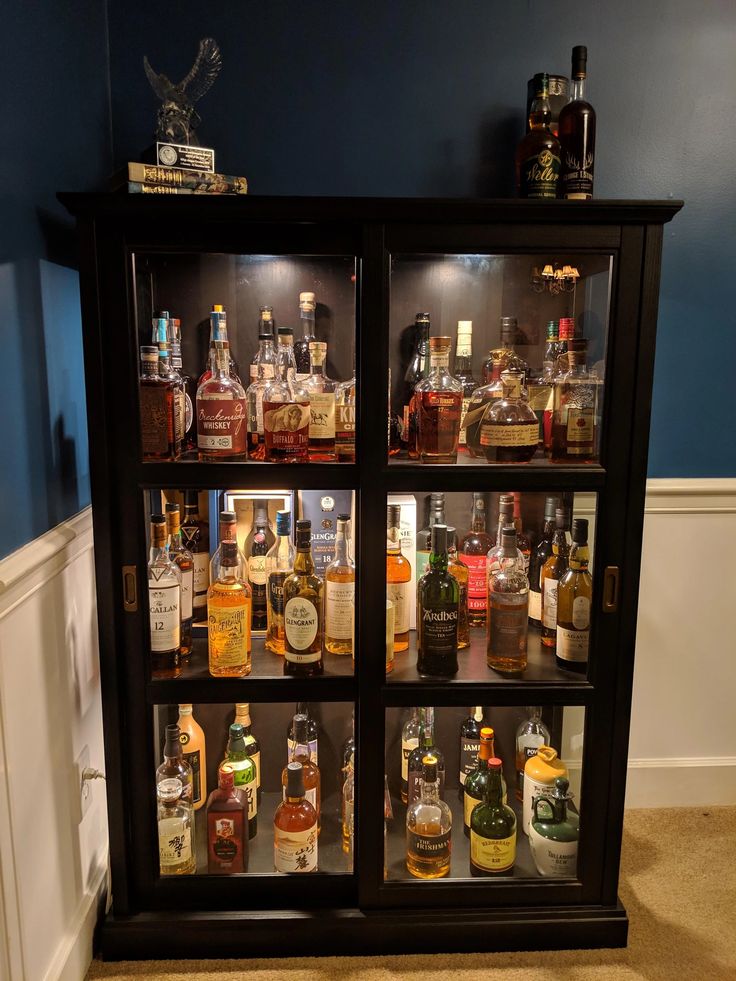 a display case filled with liquor bottles in a room next to a wall painted blue