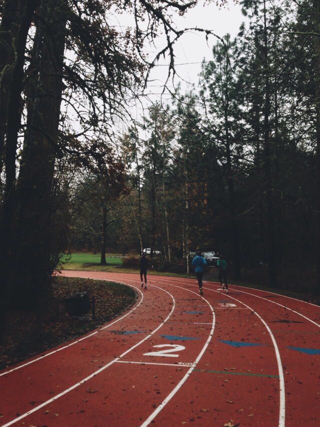 two people are running on a red track in the middle of some trees and grass