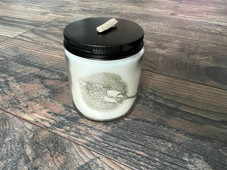 a white jar with a black lid sitting on top of a wooden floor