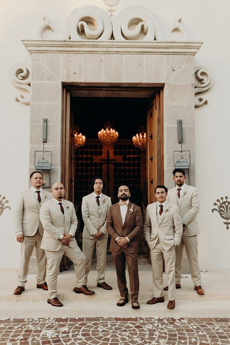 a group of men standing next to each other in front of a door with chandeliers