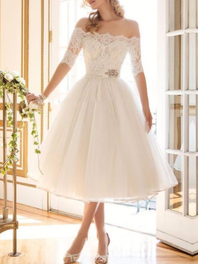 a woman in a white dress standing on a wooden floor next to a window with flowers