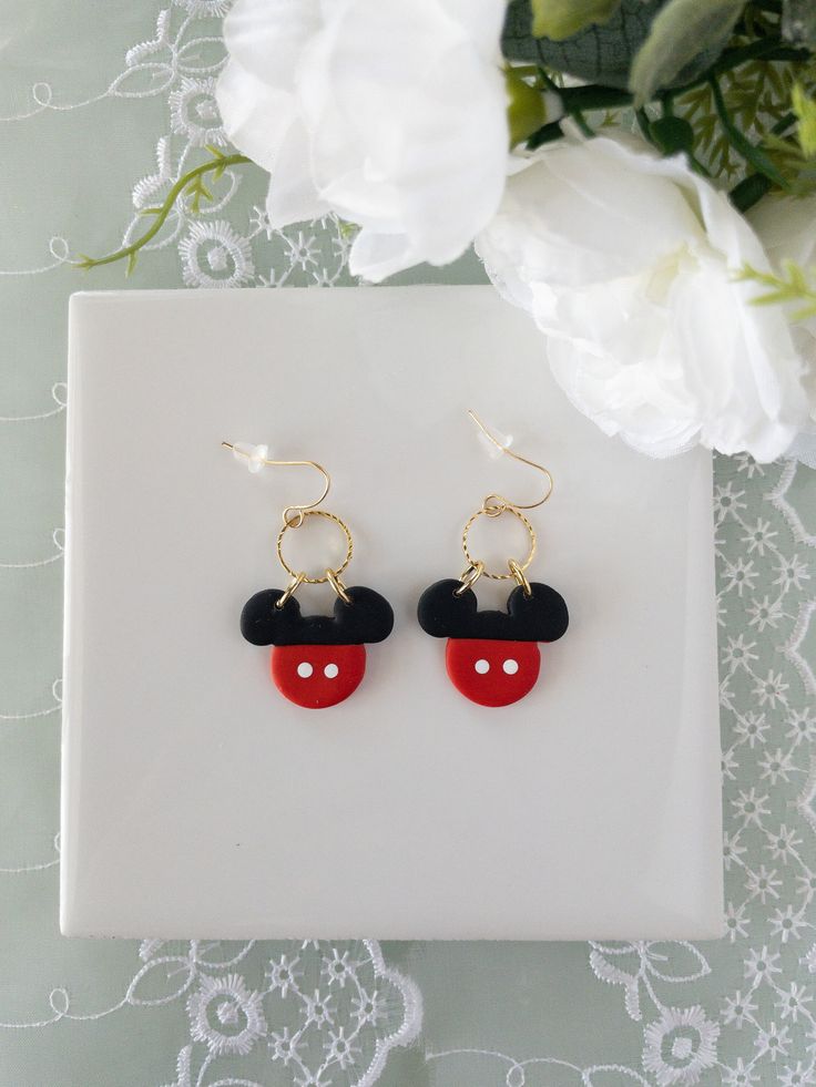 mickey mouse earring with red and black ears on a white plate next to flowers