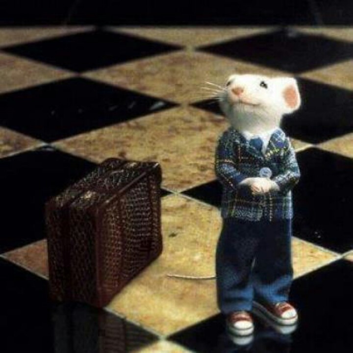 a toy mouse standing on top of a checkered floor next to a piece of luggage