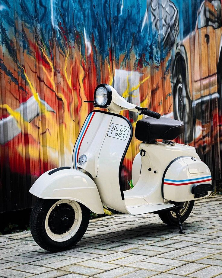 a white scooter is parked in front of a wall with graffiti on it