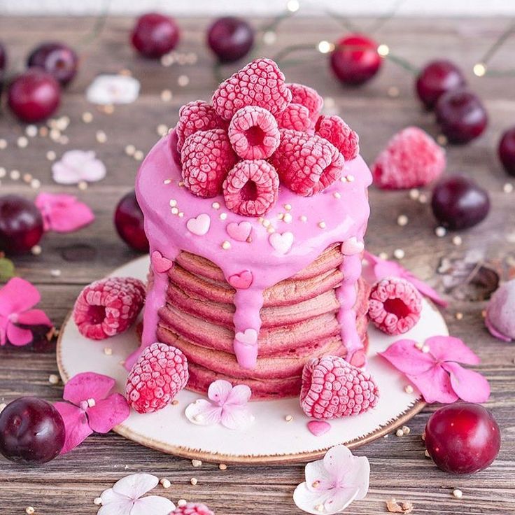 a cake with raspberries on top and pink icing is sitting on a plate