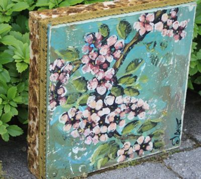 an old suitcase with flowers painted on it sitting in front of some bushes and shrubbery