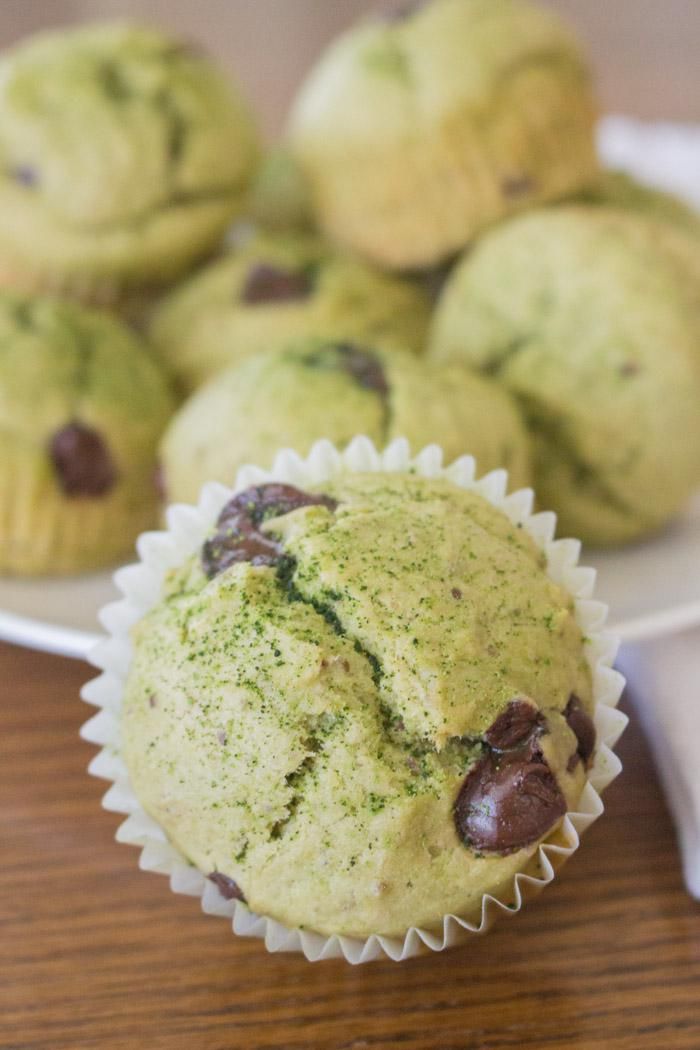 some green muffins on a white plate with chocolate chips in the middle and more muffins behind them