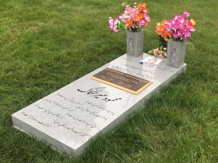 two vases with flowers sitting on top of a stone slab in the grass next to some writing