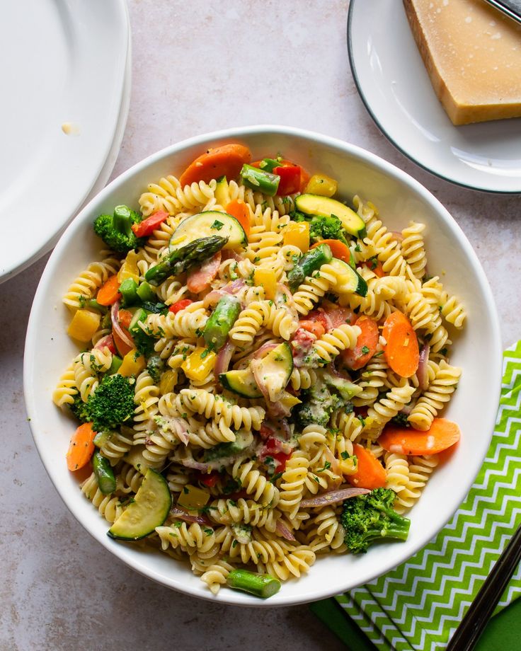 a white bowl filled with pasta salad next to plates and utensils on a table