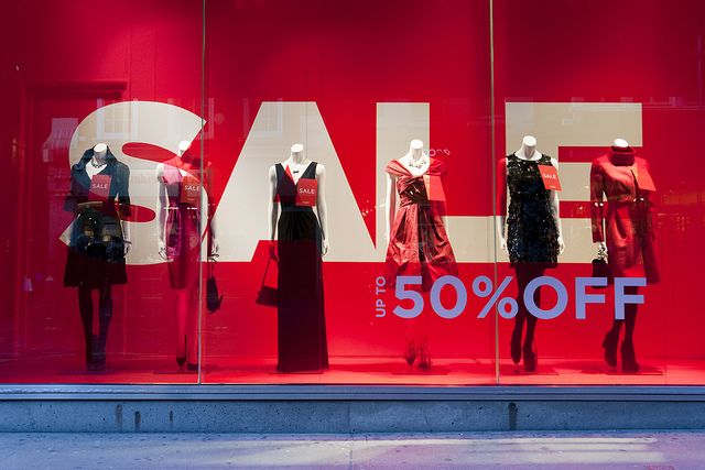 a red sale sign is in the window of a store with mannequins