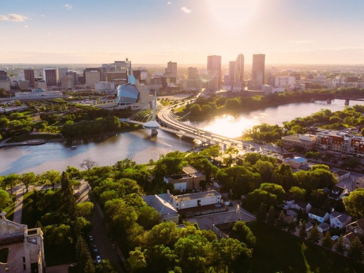 an aerial view of a city and the river in the foreground, with trees on both sides