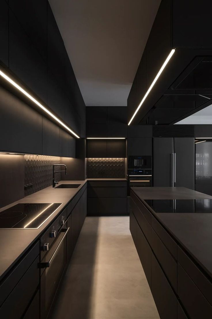 an empty kitchen with black cabinets and counter tops is lit by recessed lights above the sink