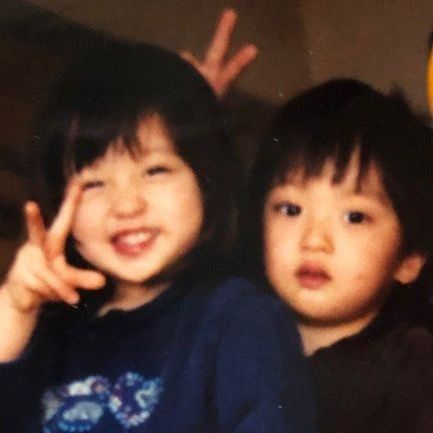 two young children standing next to each other with one pointing at the camera and smiling