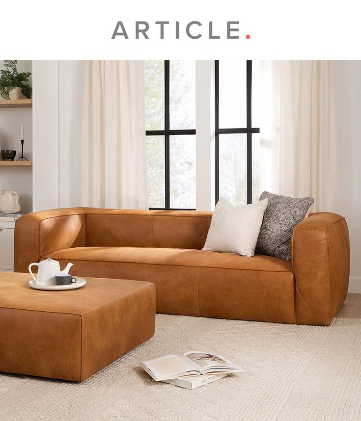 a brown leather couch sitting on top of a white rug in front of a window