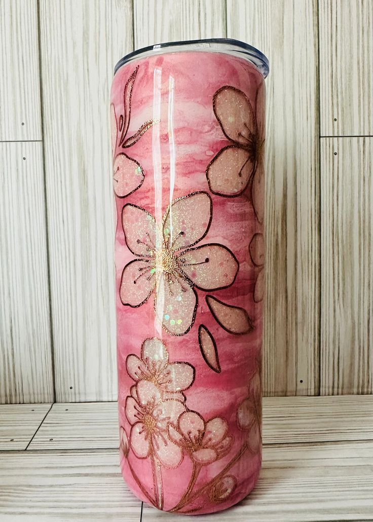 a pink tumbler with flowers painted on it sitting on a wooden table next to a wall